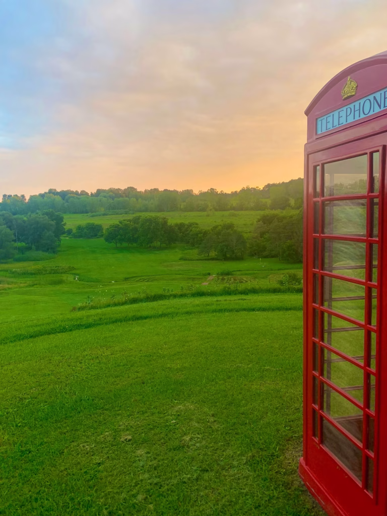 Customer Showcase Customer photo of a red British telephone booth from The Kings Bay standing in a green field at sunset